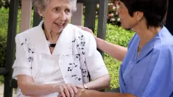 Female nurse sitting with elderly woman outdoors